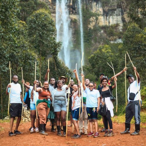 A happy group of hikers with walking sticks in front of the main Sipi Falls on Mount Elgon, Uganda