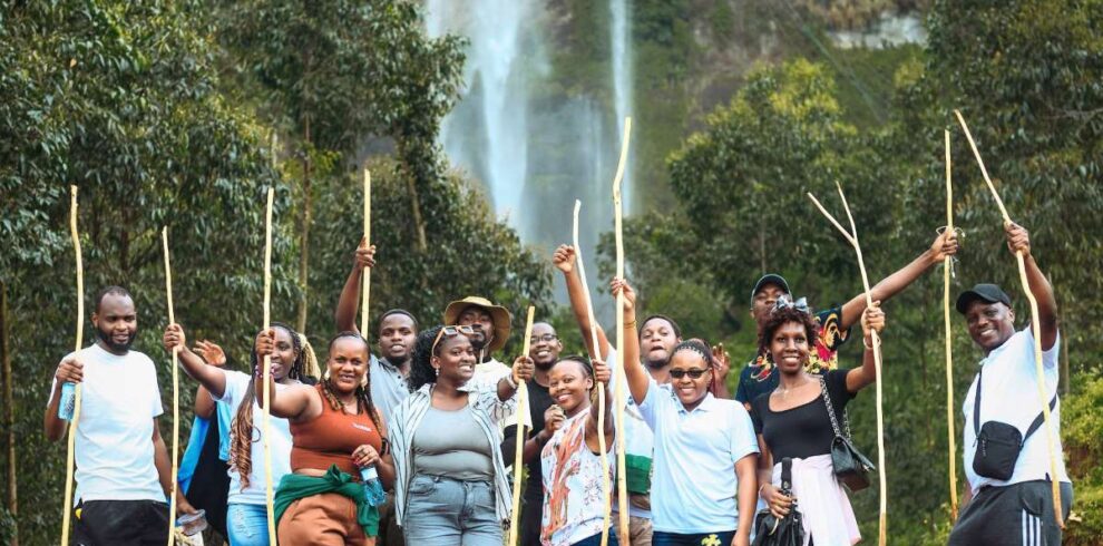 A happy group of hikers with walking sticks in front of the main Sipi Falls on Mount Elgon, Uganda