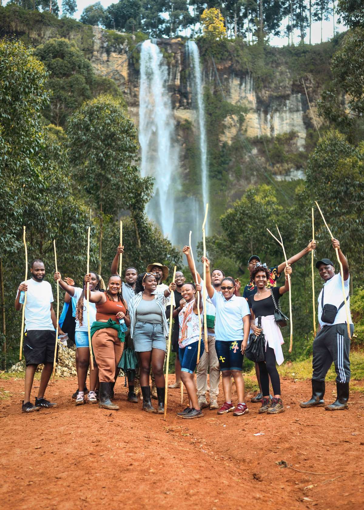 A happy group of hikers with walking sticks in front of the main Sipi Falls on Mount Elgon, Uganda